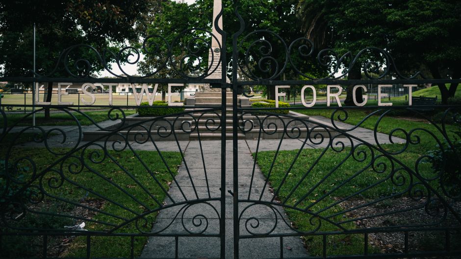 Ornate iron gate with 'Lest We Forget' in a tranquil memorial park setting.